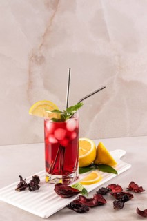 A vibrant glass of hibiscus tea with ice, garnished with lemon slices and mint. It sits on a light