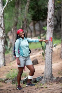 Mauritian woman, 35 years old, showing a hiking trail marker in a casuarina forest, Rodrigues