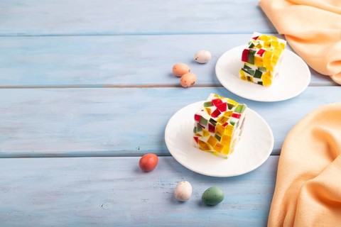 Colored Fruit and milk jelly on blue wooden background and orange linen textile, side view, copy