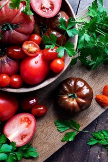 Top view of assorted tomatoes with fresh parsley on a rustic wooden board. The vibrant colors and