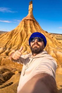 Bearded tourist in sunglasses and blue turban taking a selfie with thumbs up in front of stunning