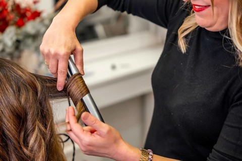 Professional hairdresser carefully styling a woman's long brunette hair with a curling iron at a