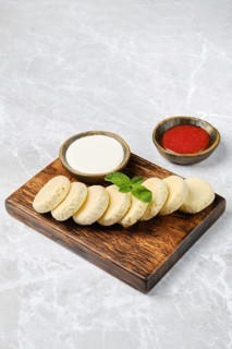 A wooden platter displays a stack of soft curd patties accompanied by bowls of sour cream and