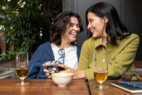 A cheerful lesbian couple sharing a moment of joy and laughter at an outdoor café. They are seated