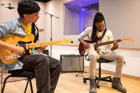Two musicians play electric guitars in a state-of-the-art recording studio. The room features