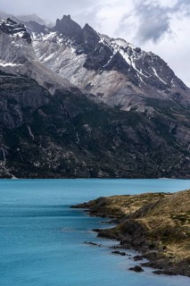 Turquoise glacial lake with rocky peninsula in the foreground, snow-capped mountain peaks and