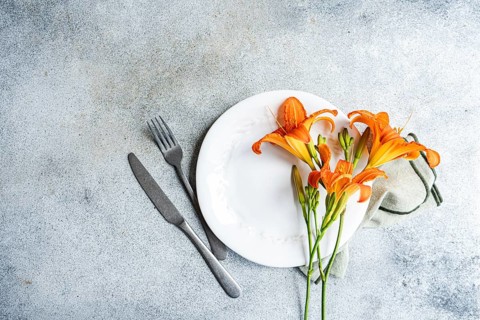 Top view of a beautiful tiger lily flower elegantly set on a white plate, accompanied by cutlery,