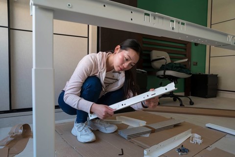 Young Asian woman focuses on assembling a white desk in her home. Engaged in a DIY furniture