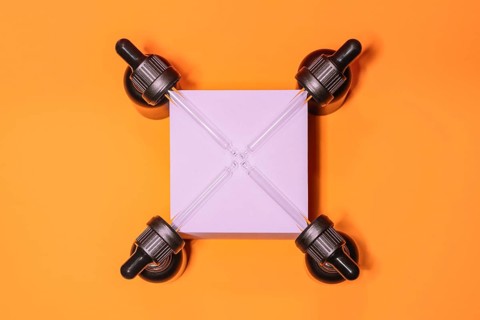 Four droppers symmetrically positioned around a pink square on a vibrant orange background,