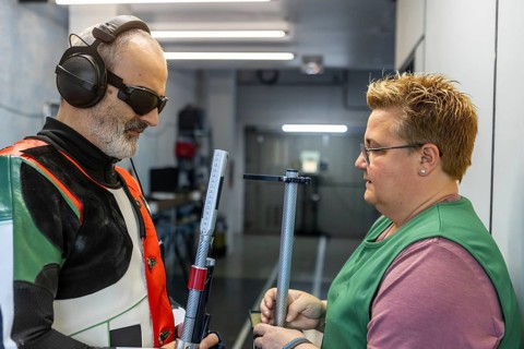 A blind athlete prepares for an Olympic shooting event with the help of a coach. Wearing protective
