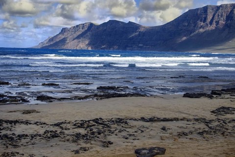 Beach with rocky coast and Famara cliffs (Risco de Famara) in the background, Caleta de Famara