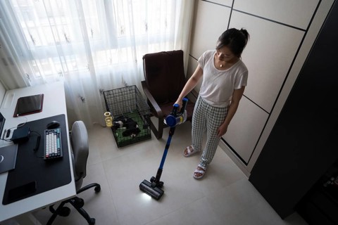 A woman efficiently vacuums the floor of a tidy home office, featuring a computer desk and a small