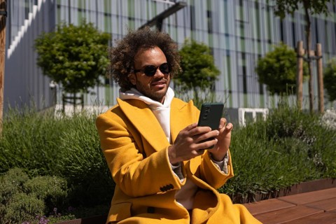 Afro man wearing sunglasses and a bright yellow coat sits on a bench, enjoying the outdoors and