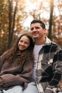 A father and daughter share a warm moment, surrounded by the vibrant colors of autumn leaves in a
