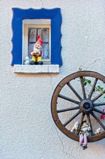 Garden gnomes on a small window and in a wooden wagon wheel on a house wall, decoration, Steinau an