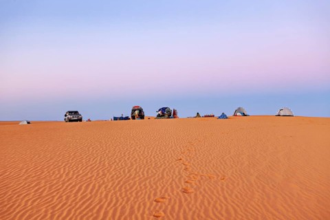 Cars and tents on a sand dune at sunrise with soft pastel colours in the sky, camping in the sand