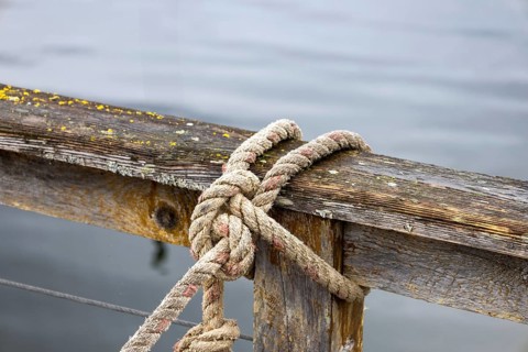 Detailed image of an old, weathered wooden dock with a sturdy rope tied in a knot, set against a