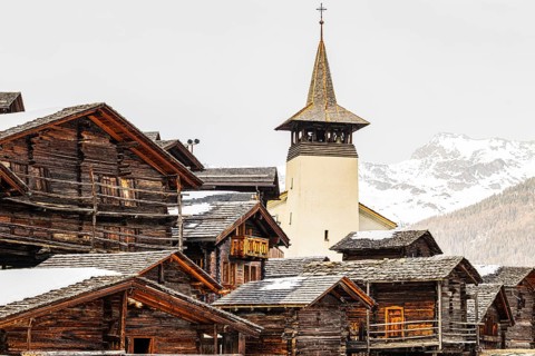 Snow-covered roofs of old farmhouses and barn storage, behind the church tower of the Saint
