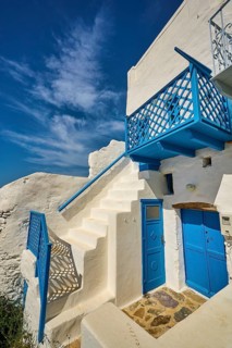 White staircase with blue railing and doors, traditional Greek house under blue sky, Chora,