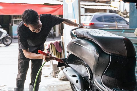 A motorcycle cleaner meticulously washes a scooter at a workshop, ensuring it's spotless. Uses a
