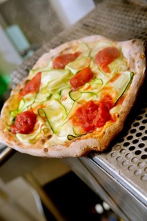 A freshly baked vegetable pizza topped with zucchini, tomato, and cheese rests on a metallic oven