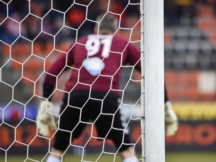 Detail of goal's post with net and football goalkeeper in the background.