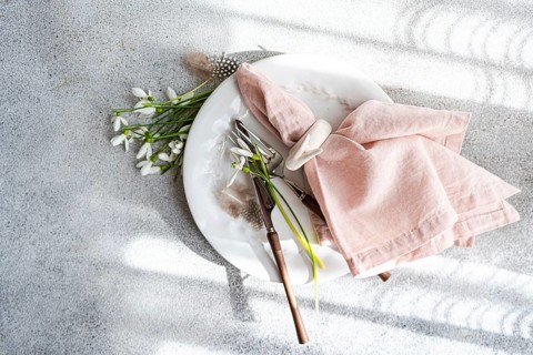 From above, an elegant table setting featuring spring snowdrops, pink napkin, and vintage cutlery