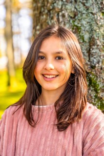 Close-up vertical portrait of a caucasian smiling girl with pink clothes enjoying nature leaning on