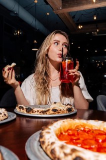 Woman sipping a refreshing berry lemonade and savoring wood-fired pepperoni pizza in a cozy, modern