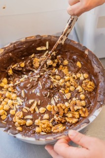 A large bowl contains melted chocolate and various nuts that are mixed together, Production Burch