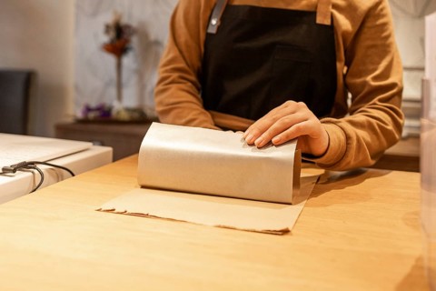 A worker wearing an apron wraps products in a cosmetics store. The focus is on their skilled hands,