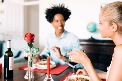 A romantic dinner scene with two people enjoying wine and a meal. A red rose and candle set the