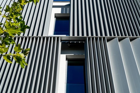 Modern architecture detail showing silver metallic stripes and blue windows among green leaves