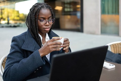 An African American businesswoman with braids enjoys a coffee break outdoors while working remotely