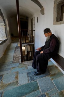 Elderly monk in traditional dress sitting on a bench in the monastery, Inside the monastery, Agiou