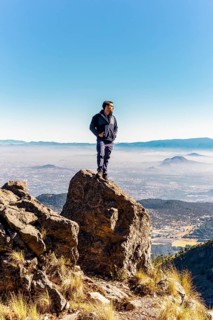 A person stands confidently on a rugged rock formation, surrounded by a stunning mountain landscape