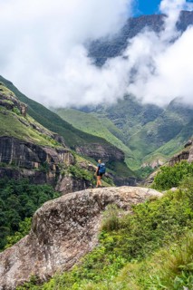 Female hiker standing in front of landscape with mountains and fog, Drakensberg National Park,