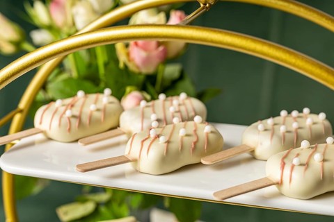 A plate of delightful dessert pop sicles coated with white chocolate, adorned with pink drizzle and