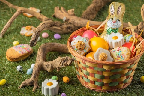 An Easter basket with chocolate bunny, colorful eggs and cookies in a meadow with wooden decoration