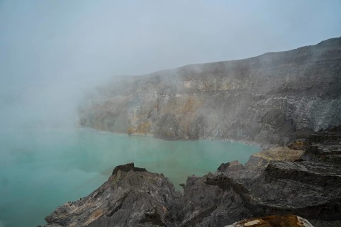 A turquoise acidic lake within the crater of Ijen volcano in Indonesia, surrounded by rocky terrain