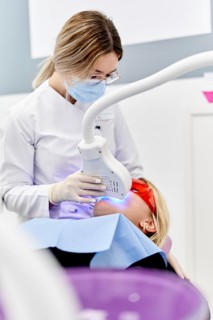 A dentist performs a teeth whitening procedure in a modern dental clinic. The patient wears