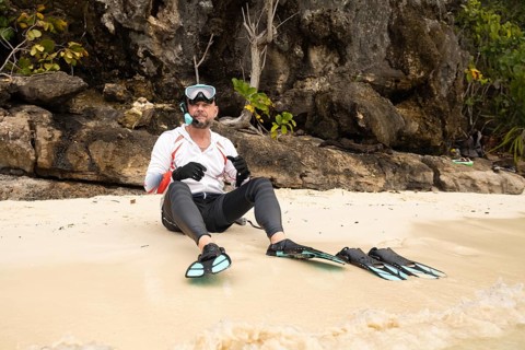 A snorkeler relaxes on the sandy beach of Raja Ampat, Indonesia, surrounded by lush greenery and