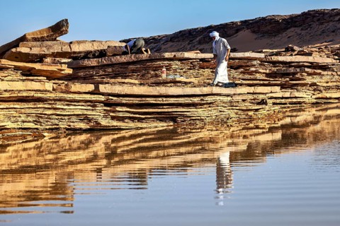 Two people walking along rocks in a reflective desert landscape, Tuareg fetching water in the