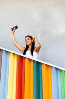 A woman wearing vibrant headphones enjoys music while standing against a backdrop of colorful