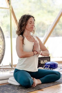A female sound therapist meditates with a large gong in the background, practicing sound therapy.