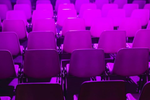 Empty rows of chairs with a vibrant purple light illuminating them at a conference of AI in