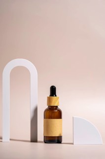 A minimalist setup featuring a brown glass dropper bottle with wooden cap, placed on a beige