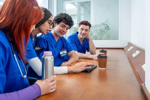 Diverse group of medical and nursing students in scrubs and stethoscopes collaborating over a