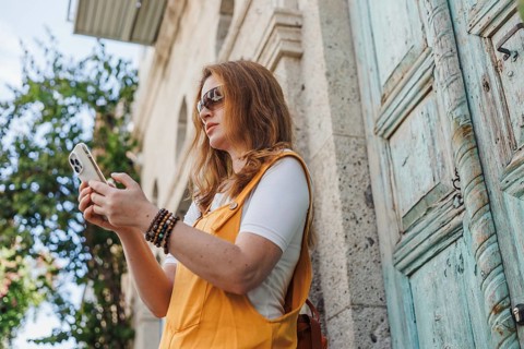 From below a mature woman, wearing orange and yellow, uses a smartphone while exploring the