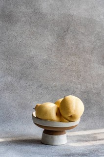 Three Chinese white pears are placed on a ceramic dish against a textured gray backdrop. The soft
